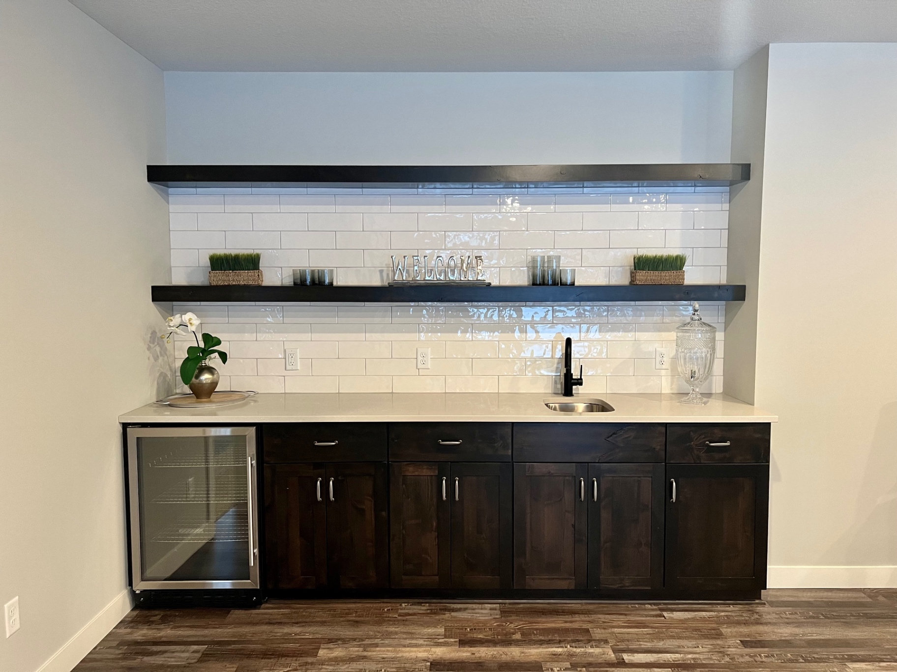 Dark cabinetry, undermount sink, and a Welcome shelf vignette.