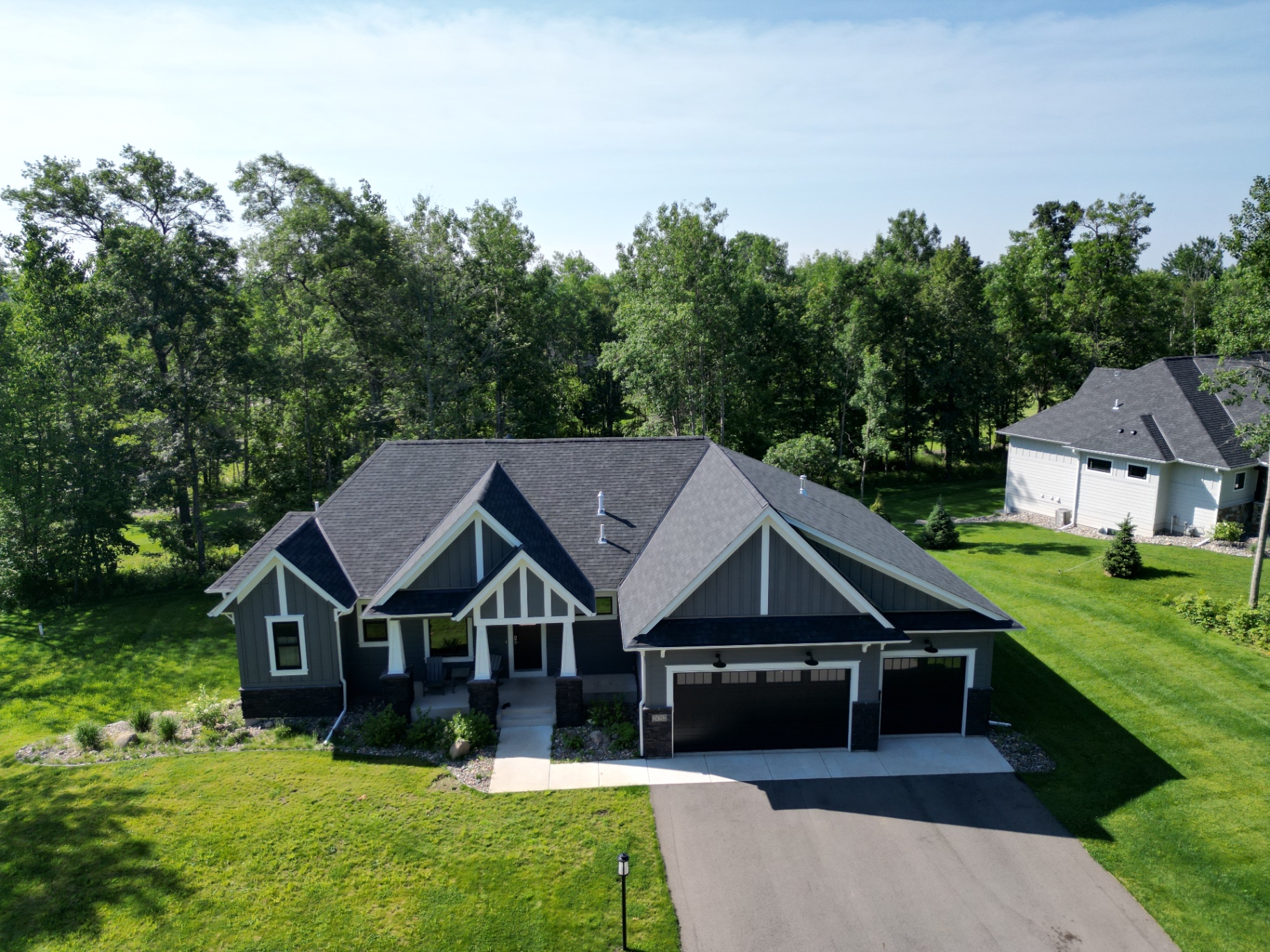 Three-car garage, stone wainscot, and twin peaks under a deep wooded backdrop.