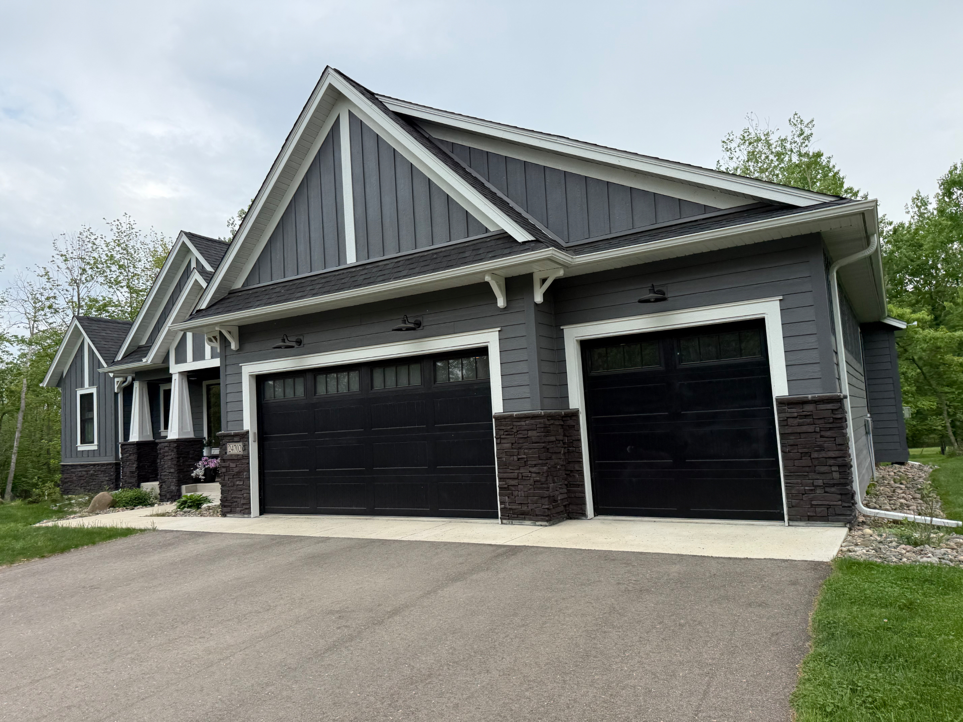 Pulling up to the three-car garage — board-and-batten gables, stacked-stone columns, and black barn-light fixtures.