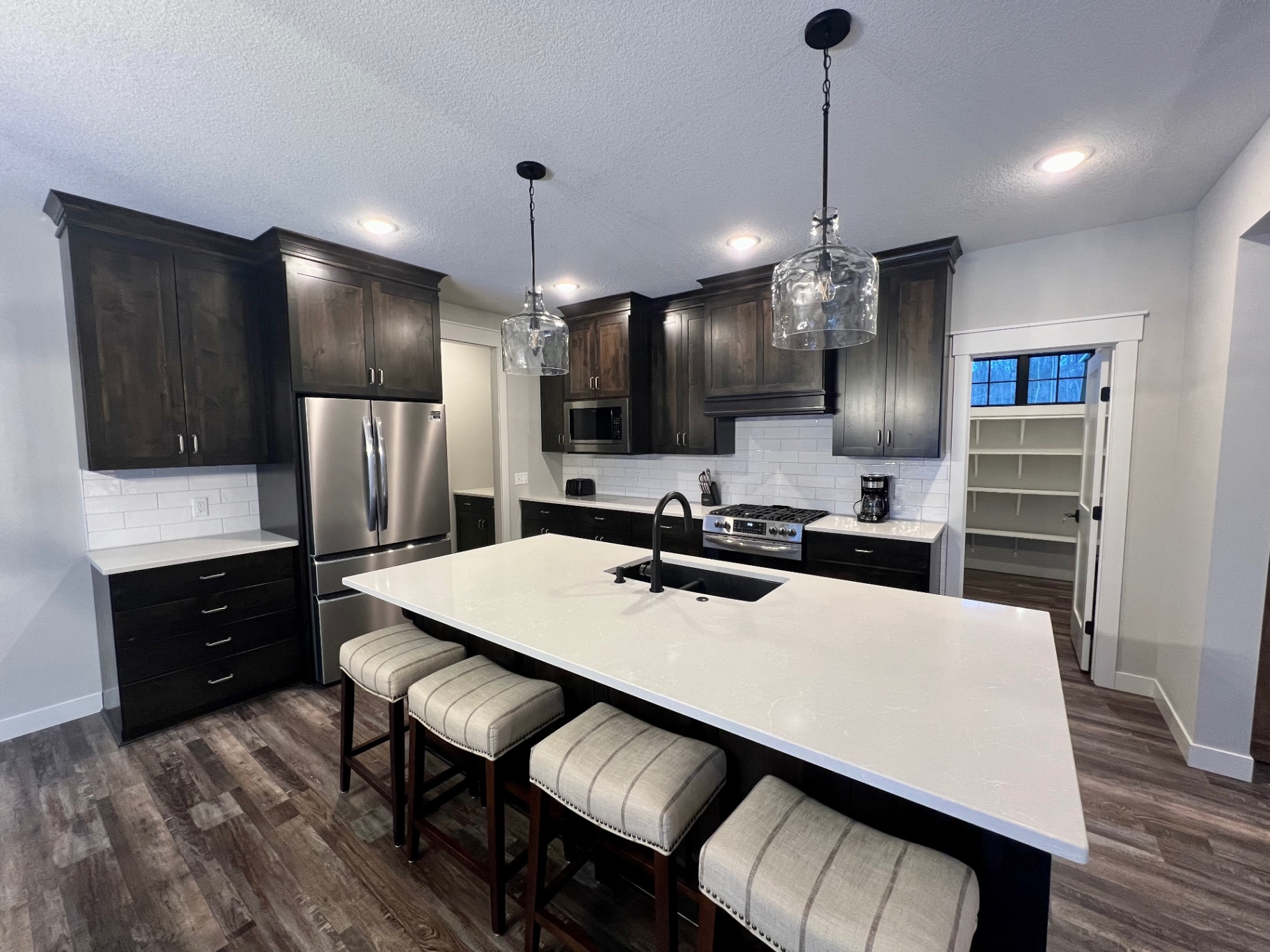 Quartz island seating four, dark stained cabinets, and statement glass pendants.